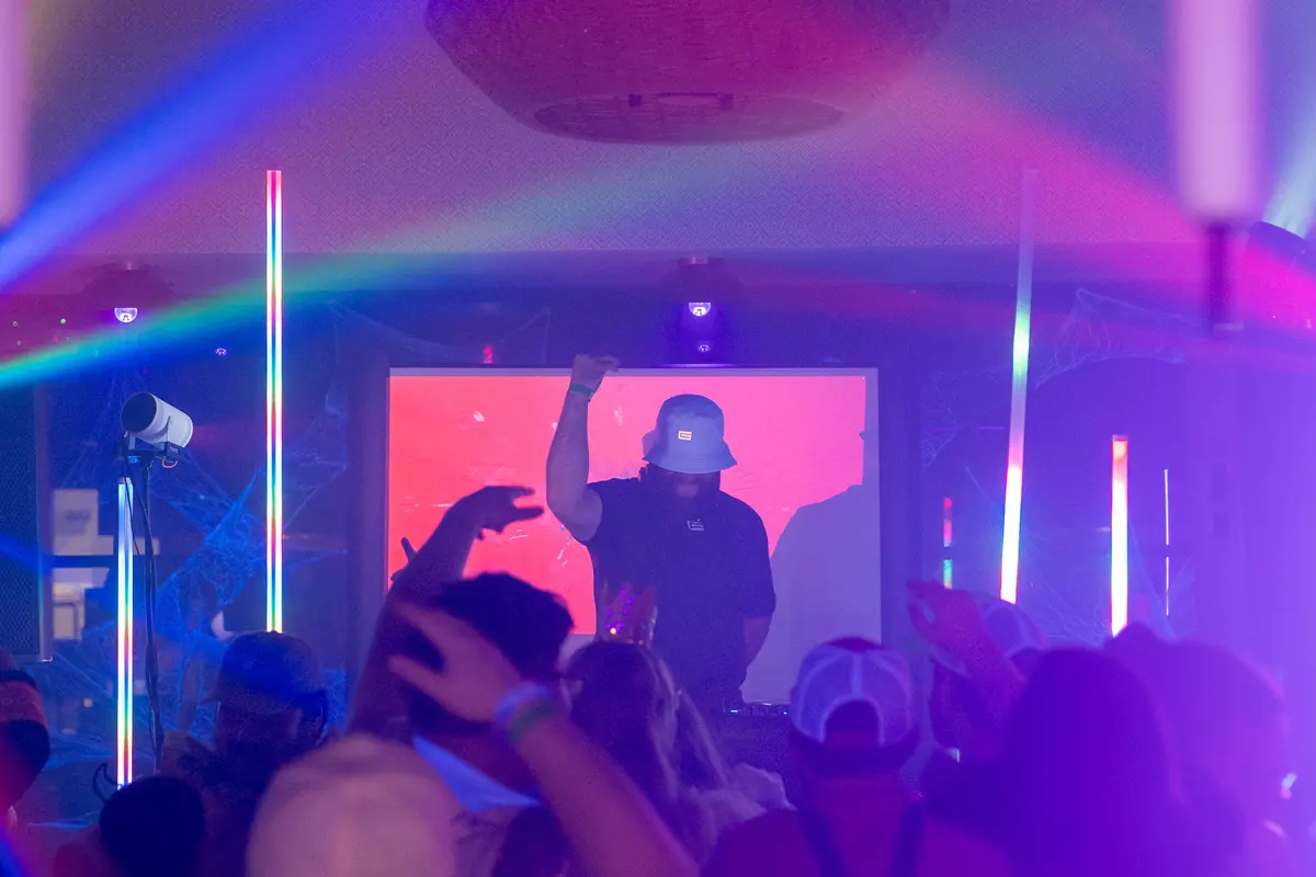 Hands up in pink and violet light as the DJ plays in front of a red screen