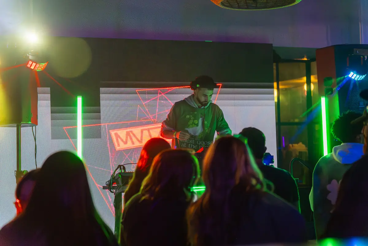The crowd seen from behind, facing the booth under green lights and red lasers