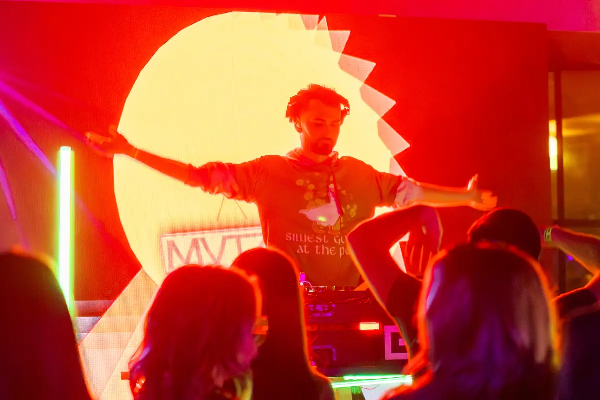 DJ with arms spread wide in front of a red and gold starburst on the LED wall as the crowd throws hands up