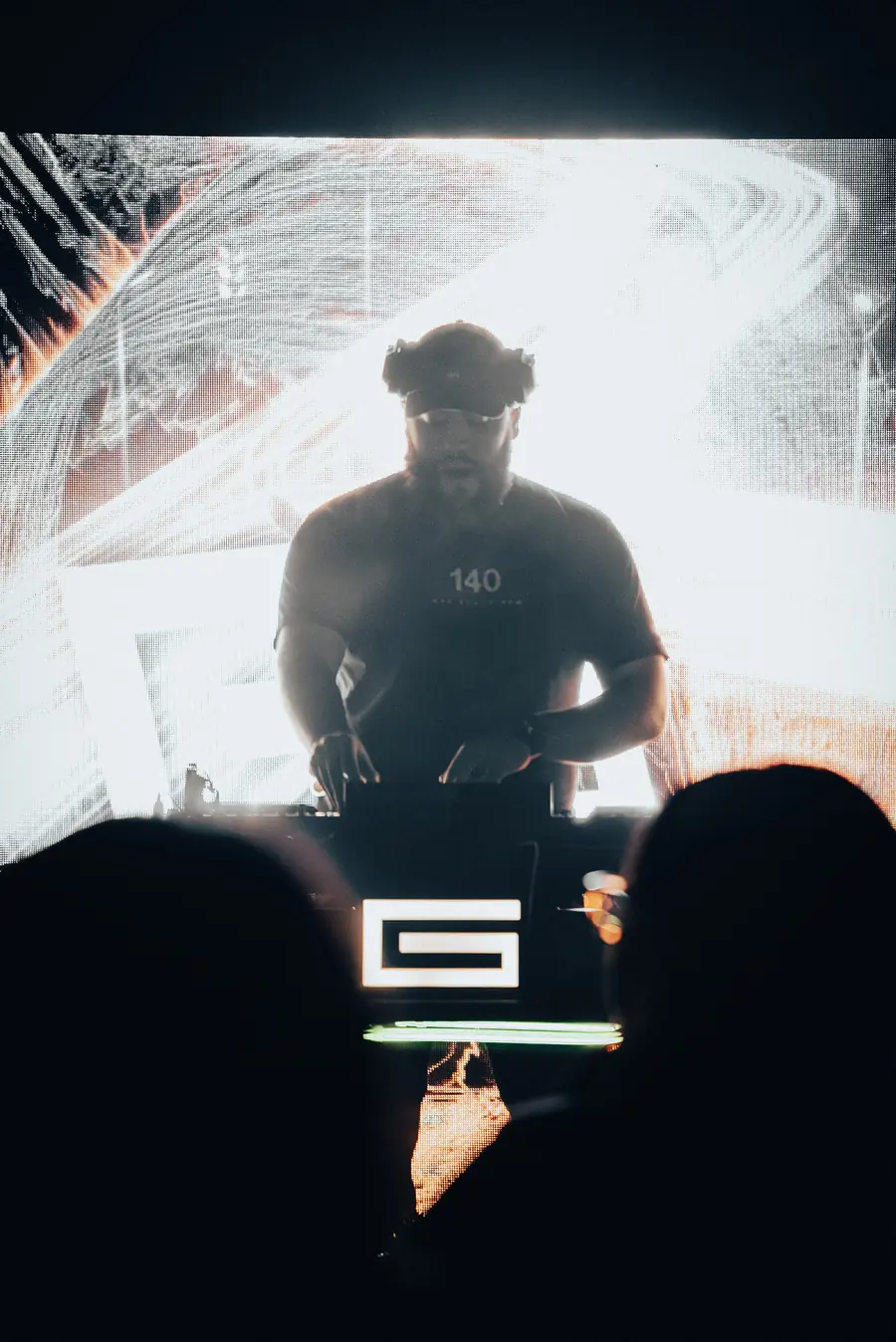 DJ silhouetted against a white LED wall, a white G lit on the front of the booth