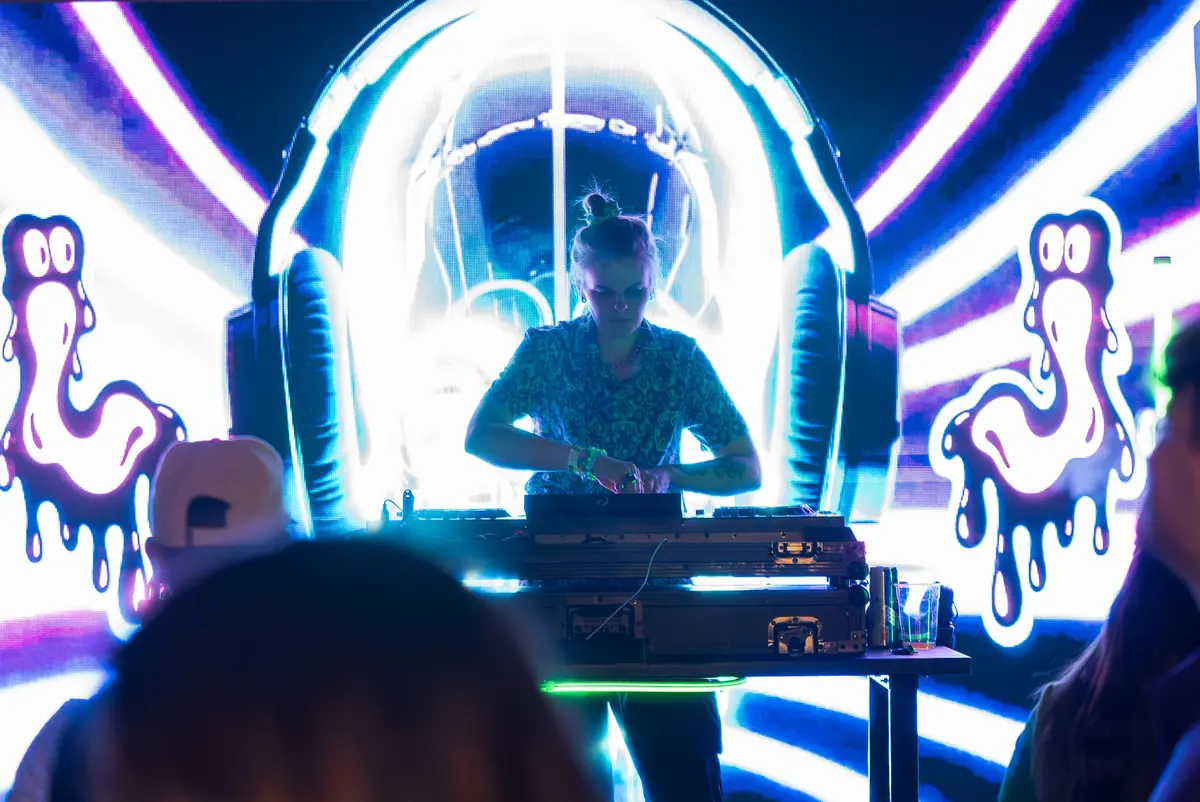 DJ at the decks framed by a giant neon headphone graphic on the LED wall